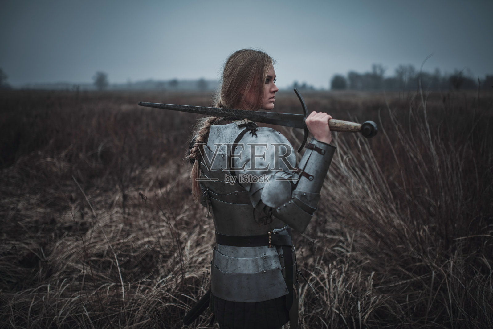 雅娜·达尔克形象中的女孩身穿盔甲，手握利剑，站在草地上。后视图。照片摄影图片