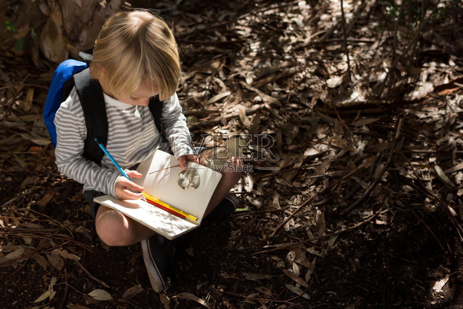 小女孩拿着背包坐在地上写笔记本照片摄影图片