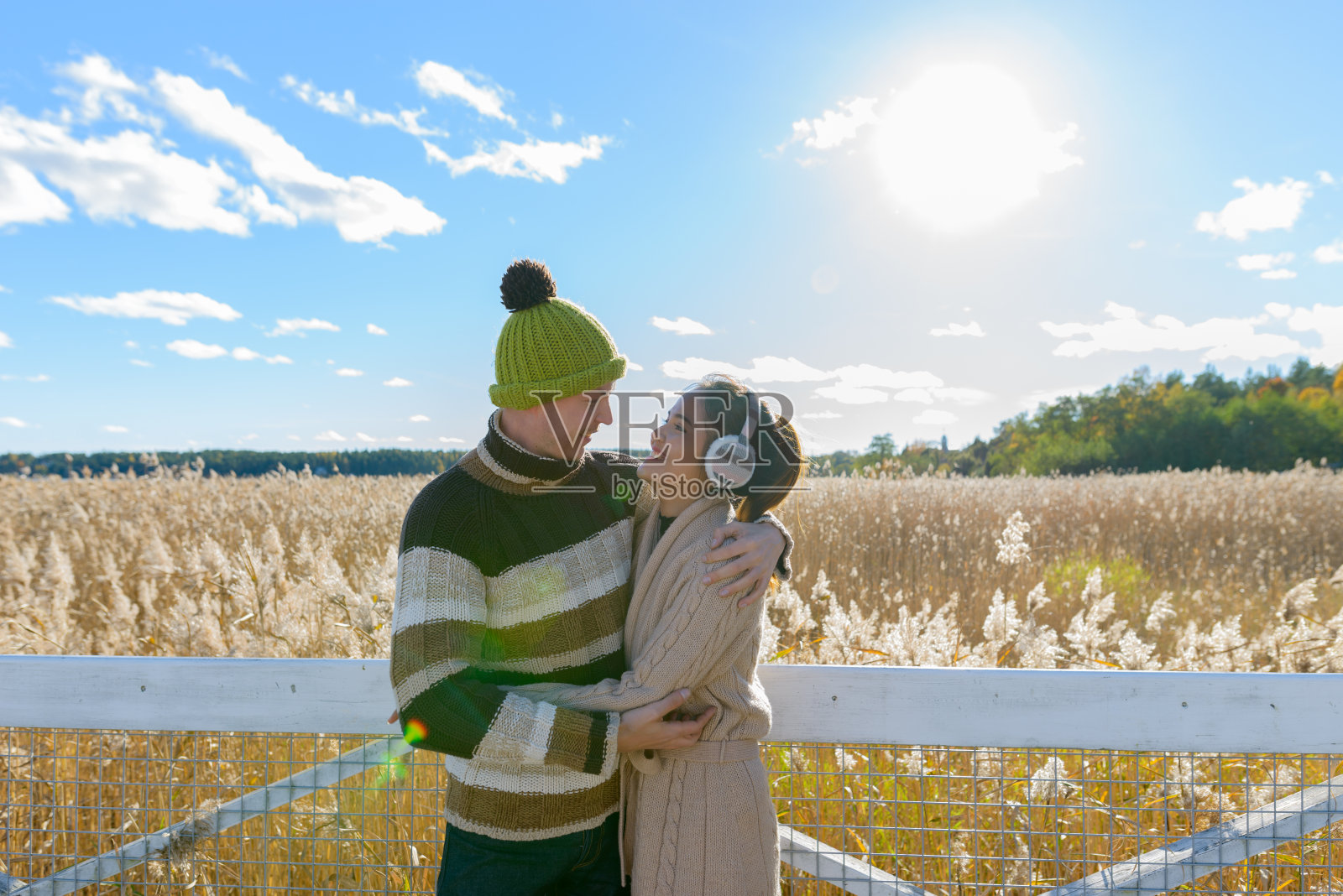 年轻幸福的夫妇微笑着拥抱，看着彼此对着风景优美的秋天芦苇田照片摄影图片