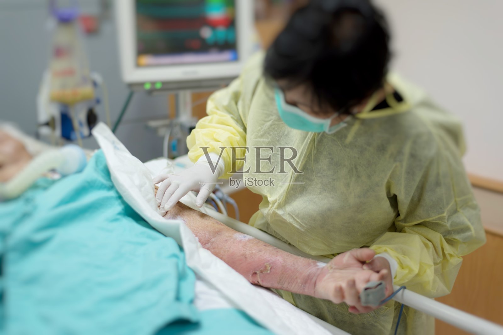 亚洲妇女40岁在隔离长袍非无菌外套是病人的亲属照顾CRE。或VRE。感染老年患者80岁，在医院病床上。照片摄影图片