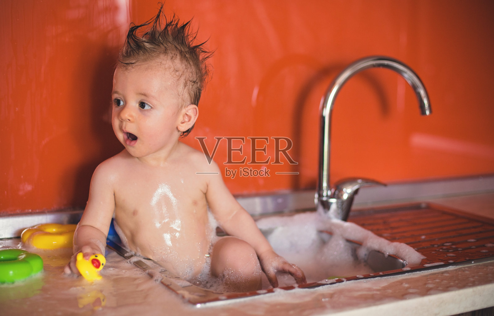 可爱的婴儿在厨房水槽洗澡照片摄影图片