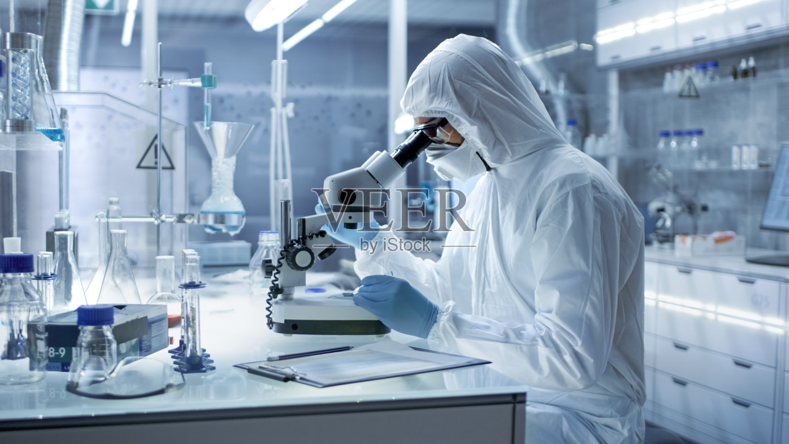 在一个安全的高水平研究实验室里，穿着工作服的科学家在显微镜下检查培养皿。照片摄影图片