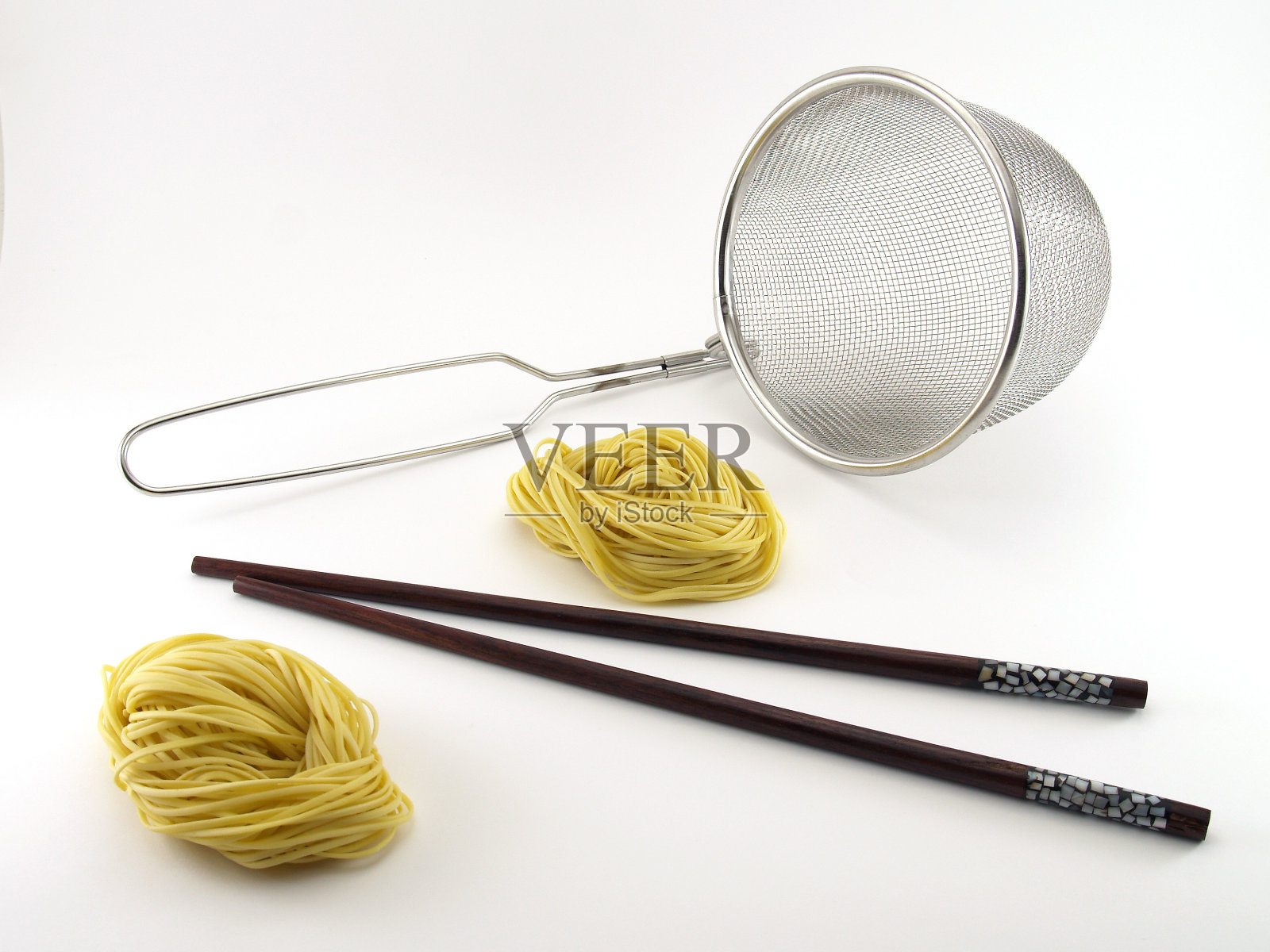 两根黄色的面条，棕色的木筷子和银色金属滤锅孤立在白色的背景上照片摄影图片