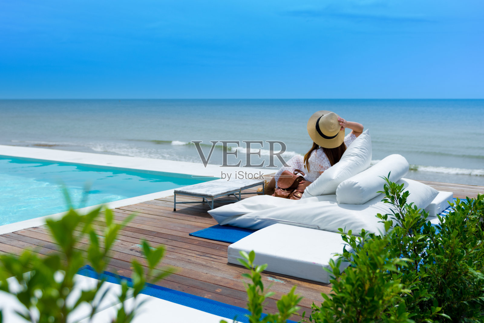 一个女人正坐在酒店游泳池前的海滩边度假。照片摄影图片