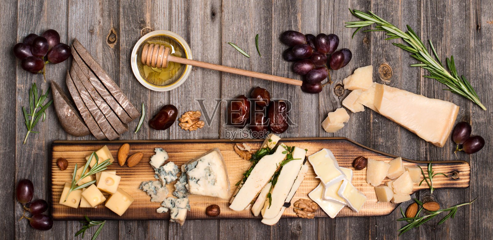 奶酪选择在木制的乡村板。奶酪拼盘与不同的奶酪，葡萄，坚果，蜂蜜和枣风化的木材背景。照片摄影图片