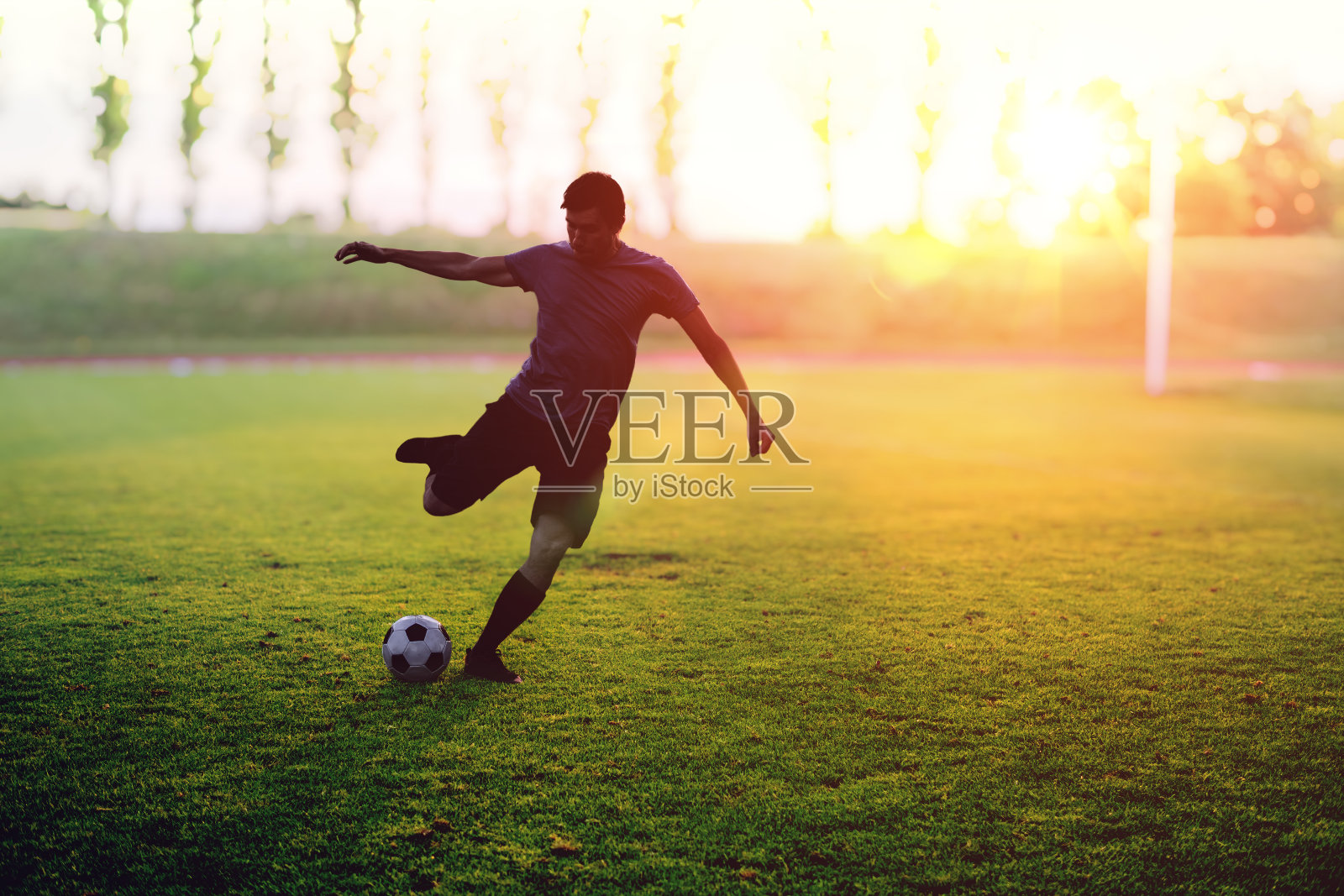 日落时分，足球运动员正在体育场投球。照片摄影图片