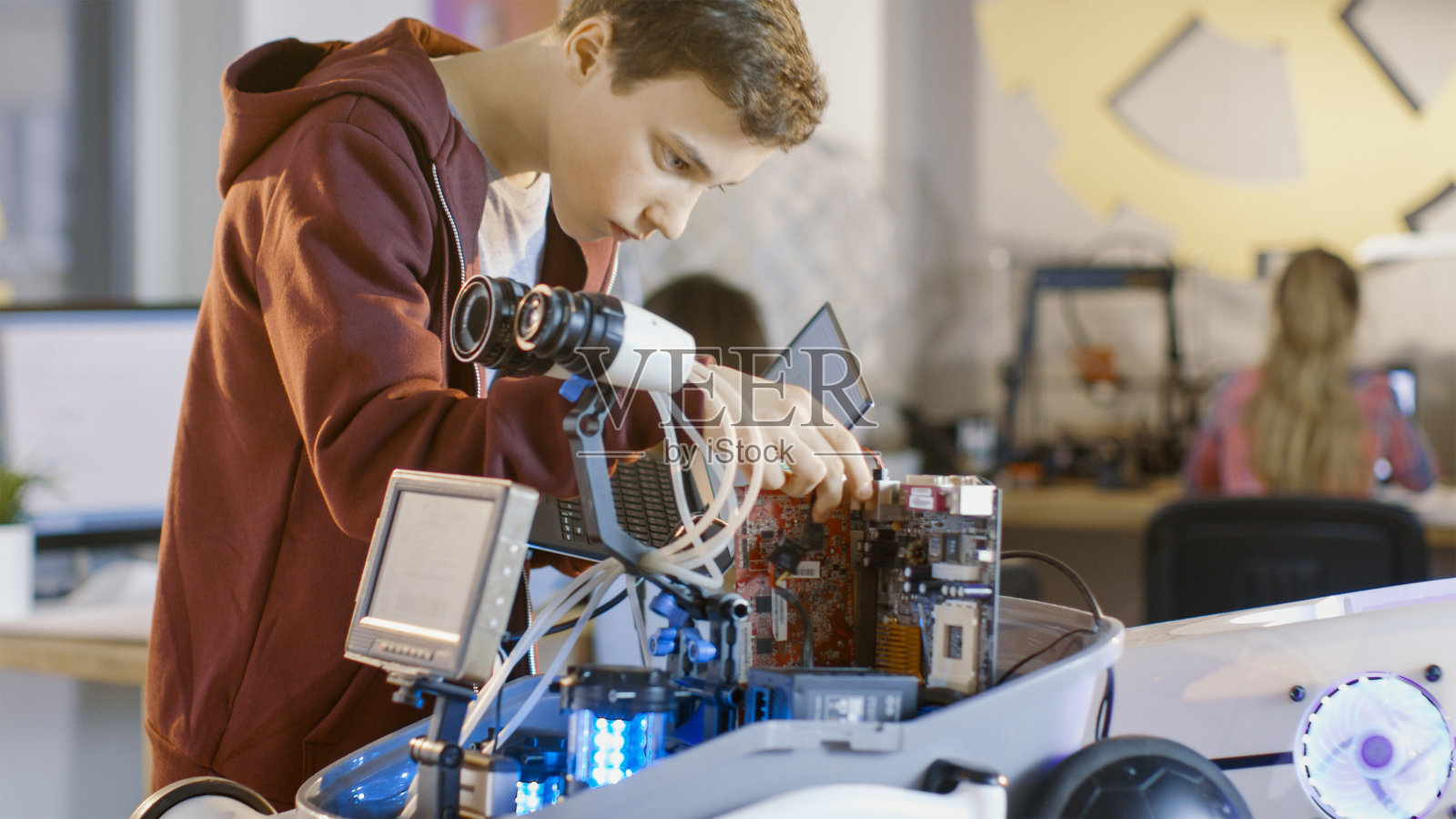 一个男孩在为他的学校机器人俱乐部项目设计一个全功能可编程机器人，带有明亮的LED灯。照片摄影图片