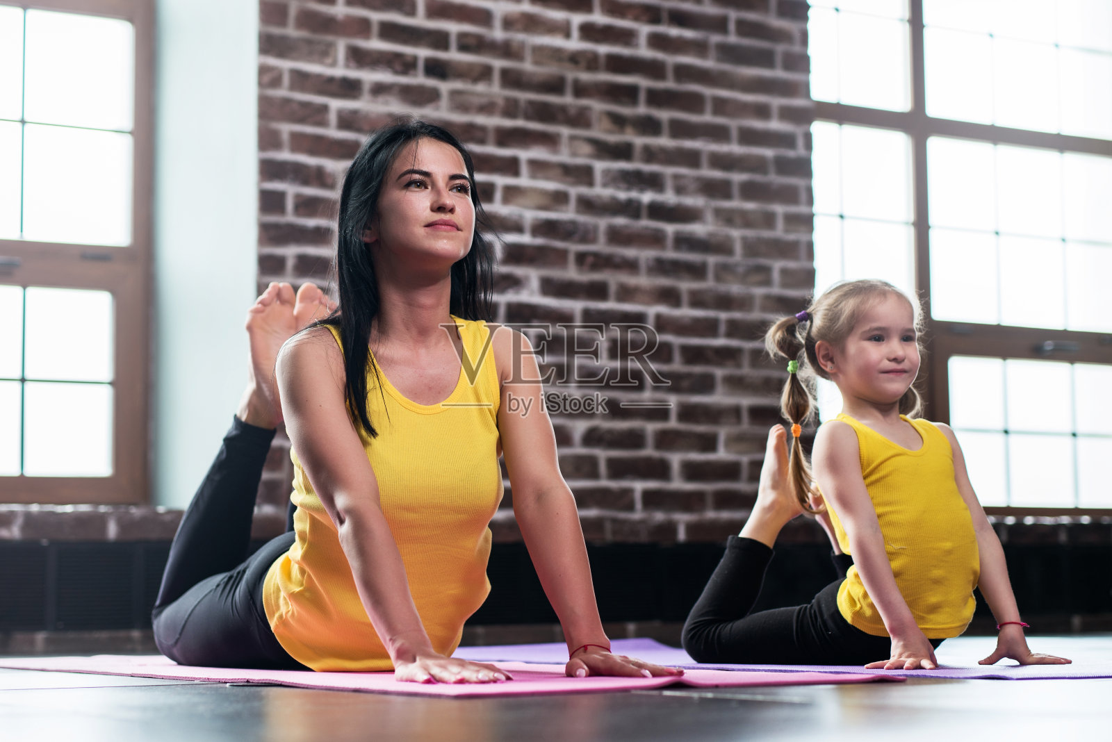 年轻的母亲和她的女儿穿着同样的运动服在集体瑜伽训练中做眼镜王蛇的姿势照片摄影图片