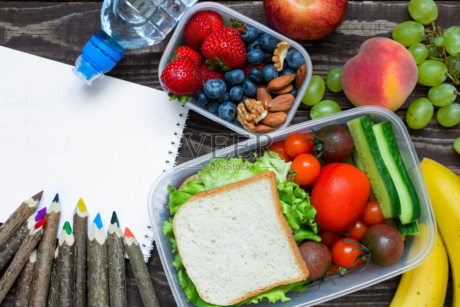 学校的午餐盒里有三明治、水果、蔬菜、瓶装水、彩色铅笔和空的抄写本照片摄影图片