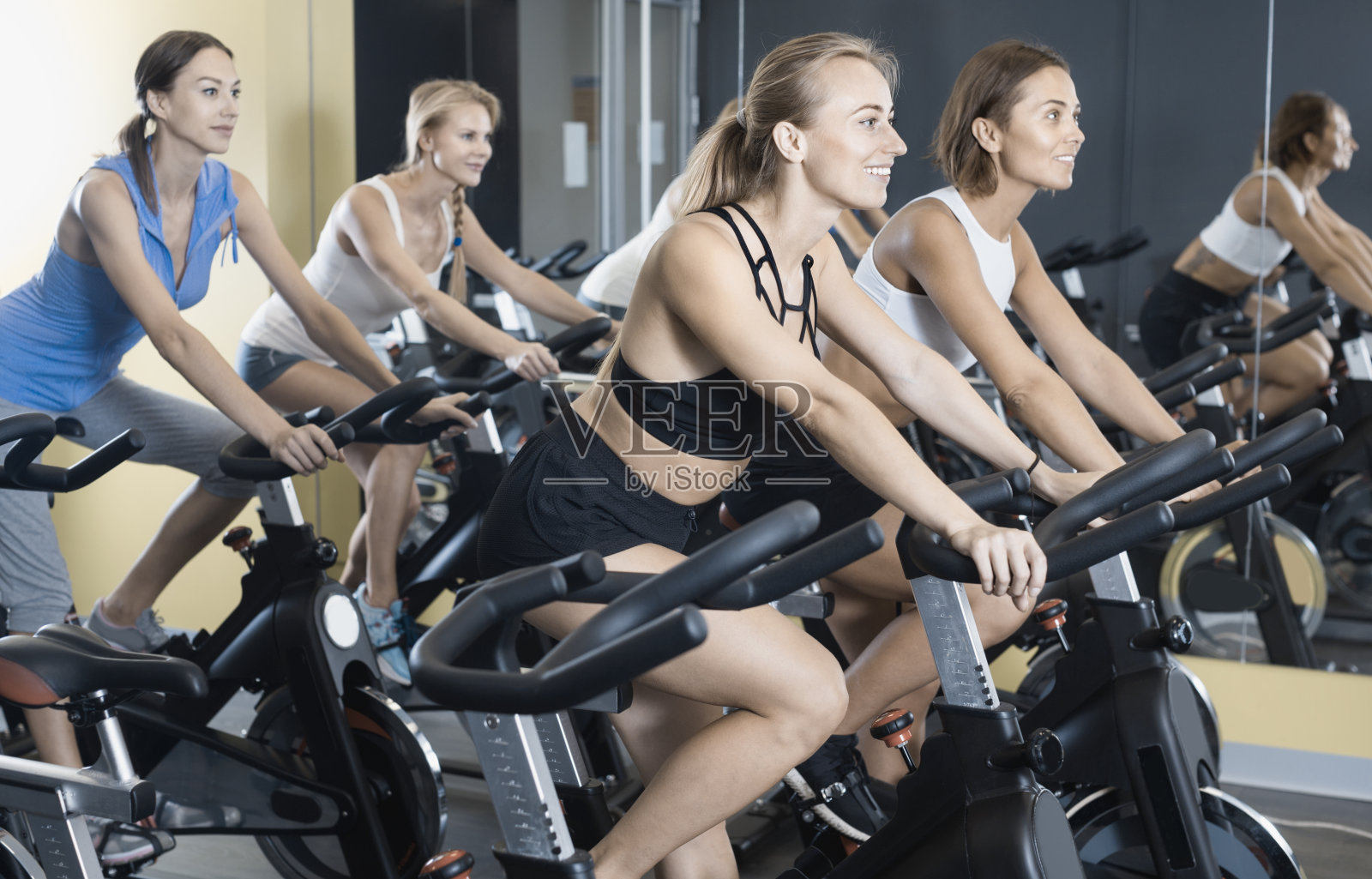女孩们在健身房里骑固定自行车锻炼照片摄影图片
