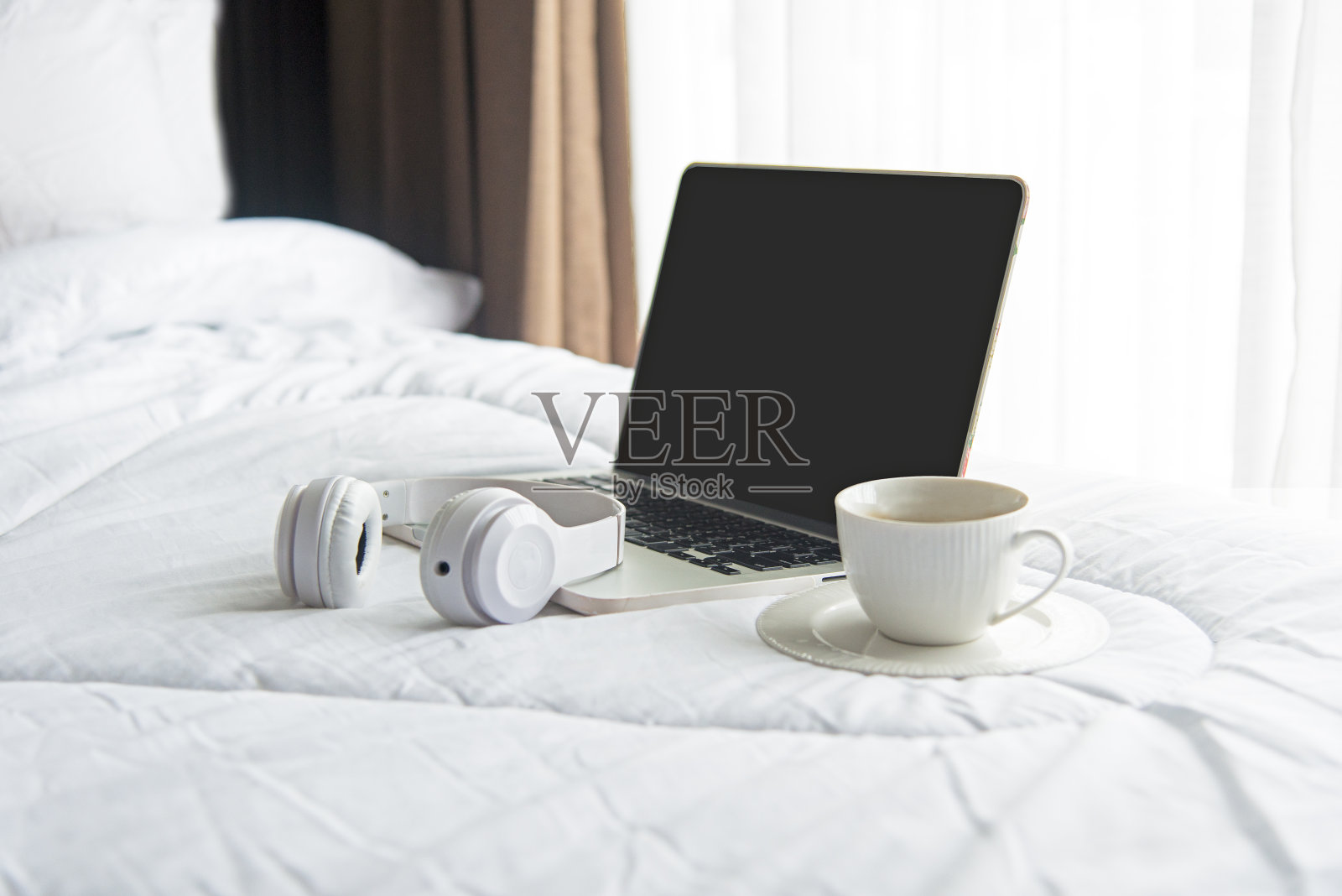 在阳光明媚的假期早晨，笔记本电脑在白色的床上工作，喝着咖啡。生活方式的概念。柔化和选择焦点照片摄影图片