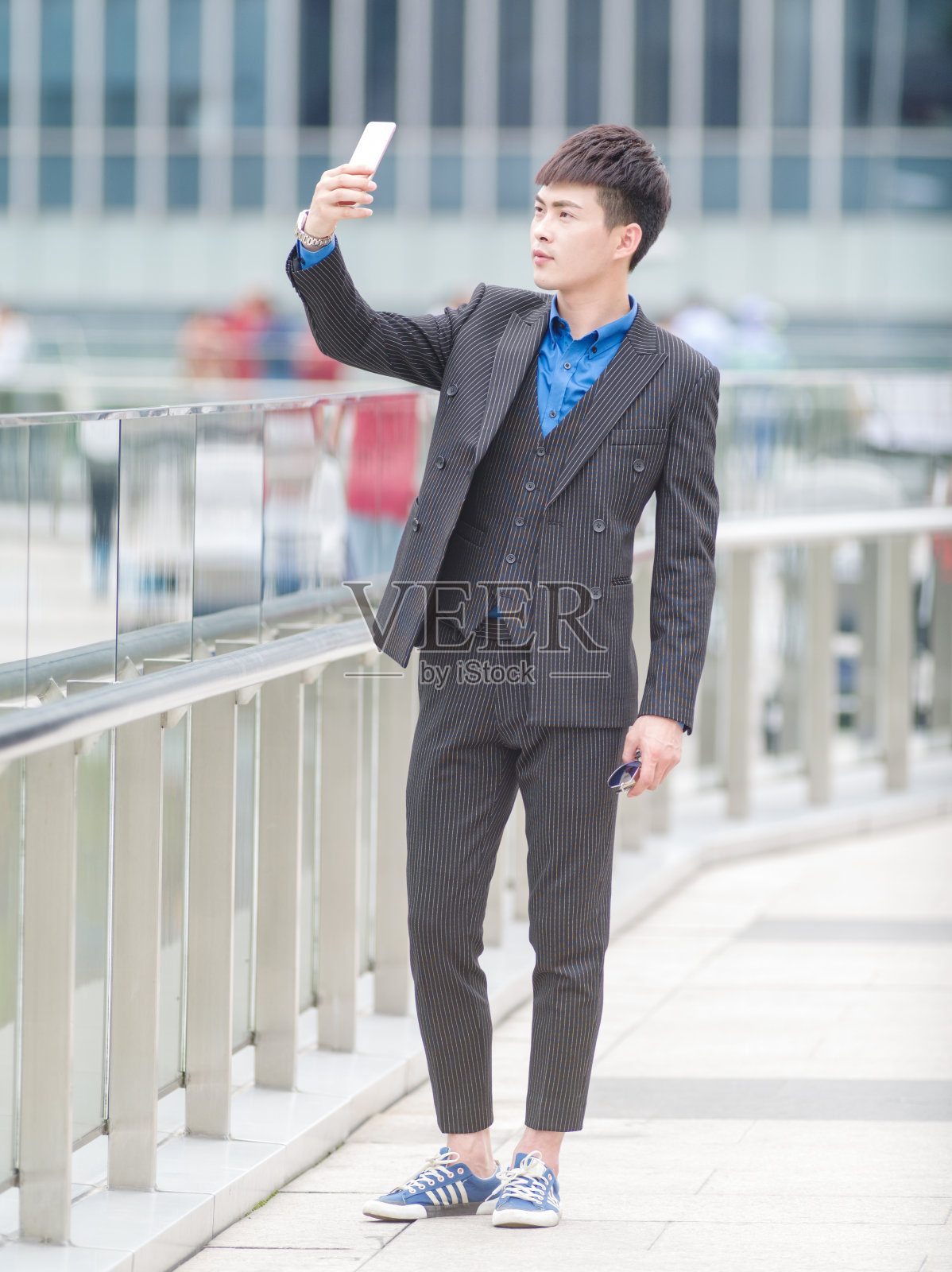 在中国上海的大街上，一名穿着西装的帅气青年正在用手机自拍。照片摄影图片