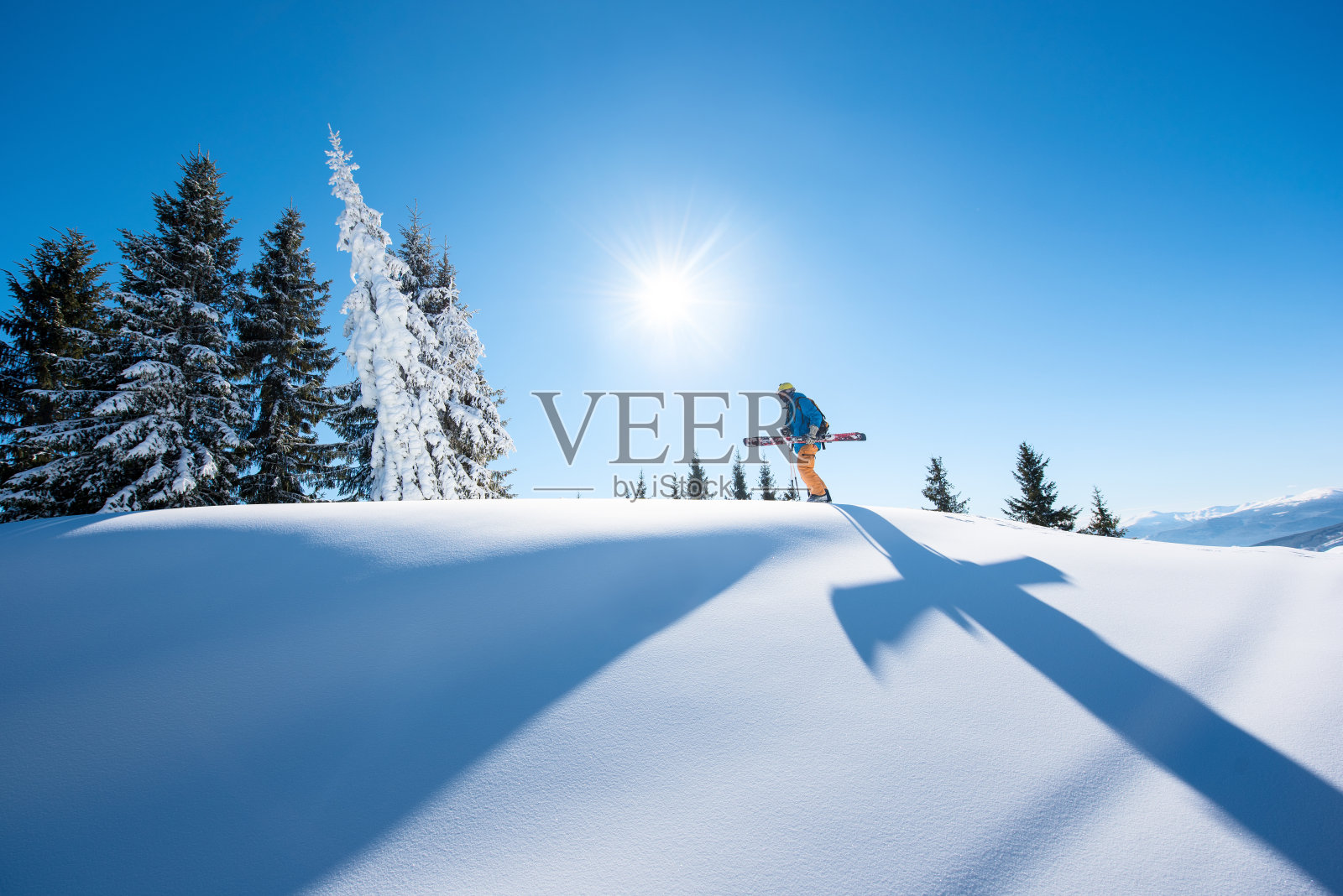 一个男性滑雪者在一个阳光明媚的冬日与他的滑雪板走在山顶上的低角度的镜头，阳光自然，娱乐，滑雪度假村的生活方式，运动的概念照片摄影图片