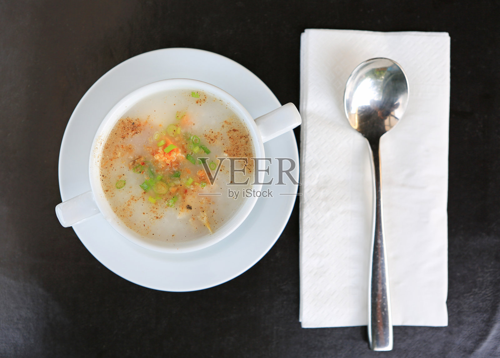 俯视图传统泰国粥米粥杯在黑色皮革盘子与勺子和纸巾。照片摄影图片