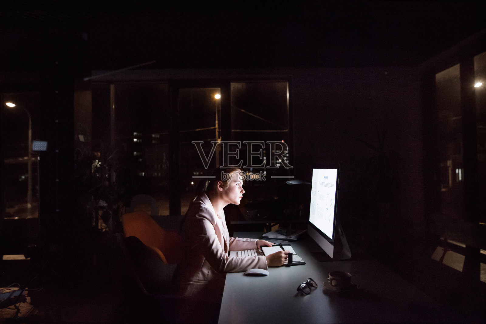 女商人晚上坐在办公室的电脑屏幕前。照片摄影图片