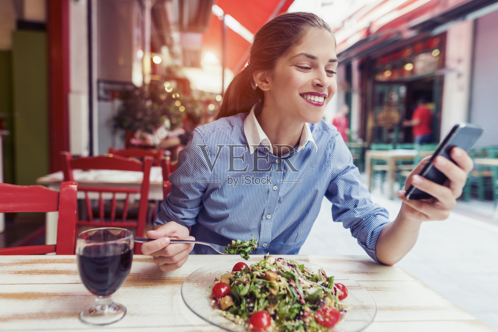 美丽的年轻女子一边吃沙拉一边用手机应用程序发送短信照片摄影图片