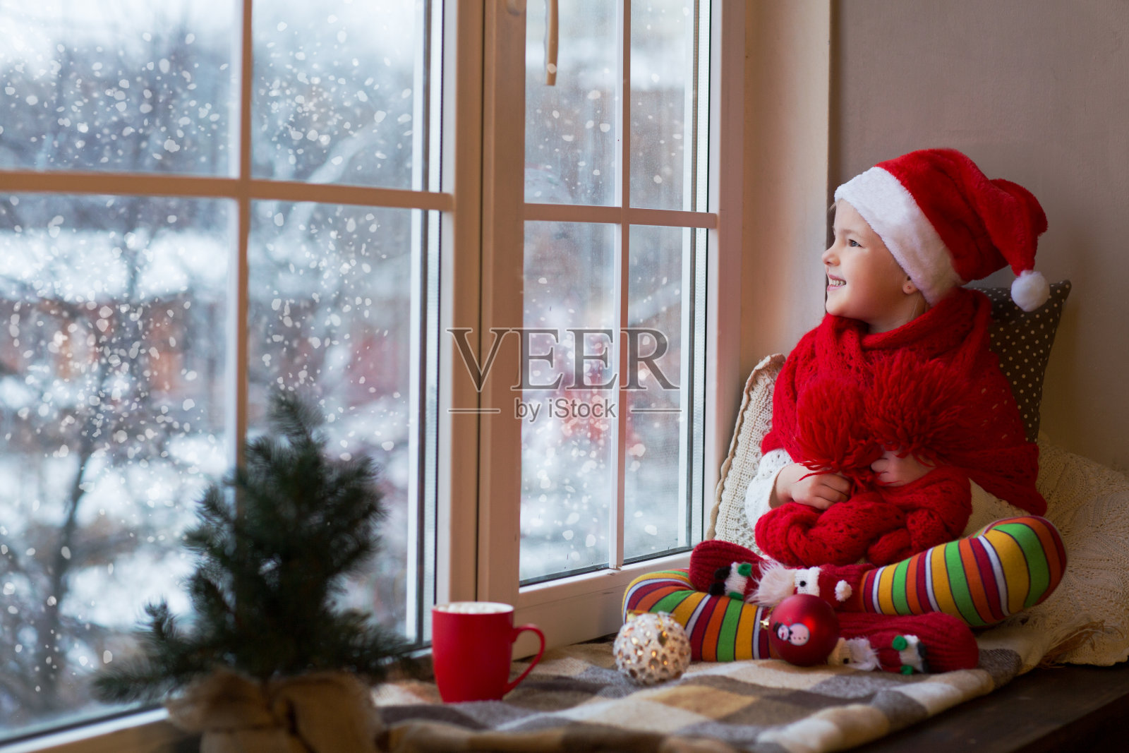 可爱的小女孩坐在窗边看雪。房间在圣诞节装饰。照片摄影图片