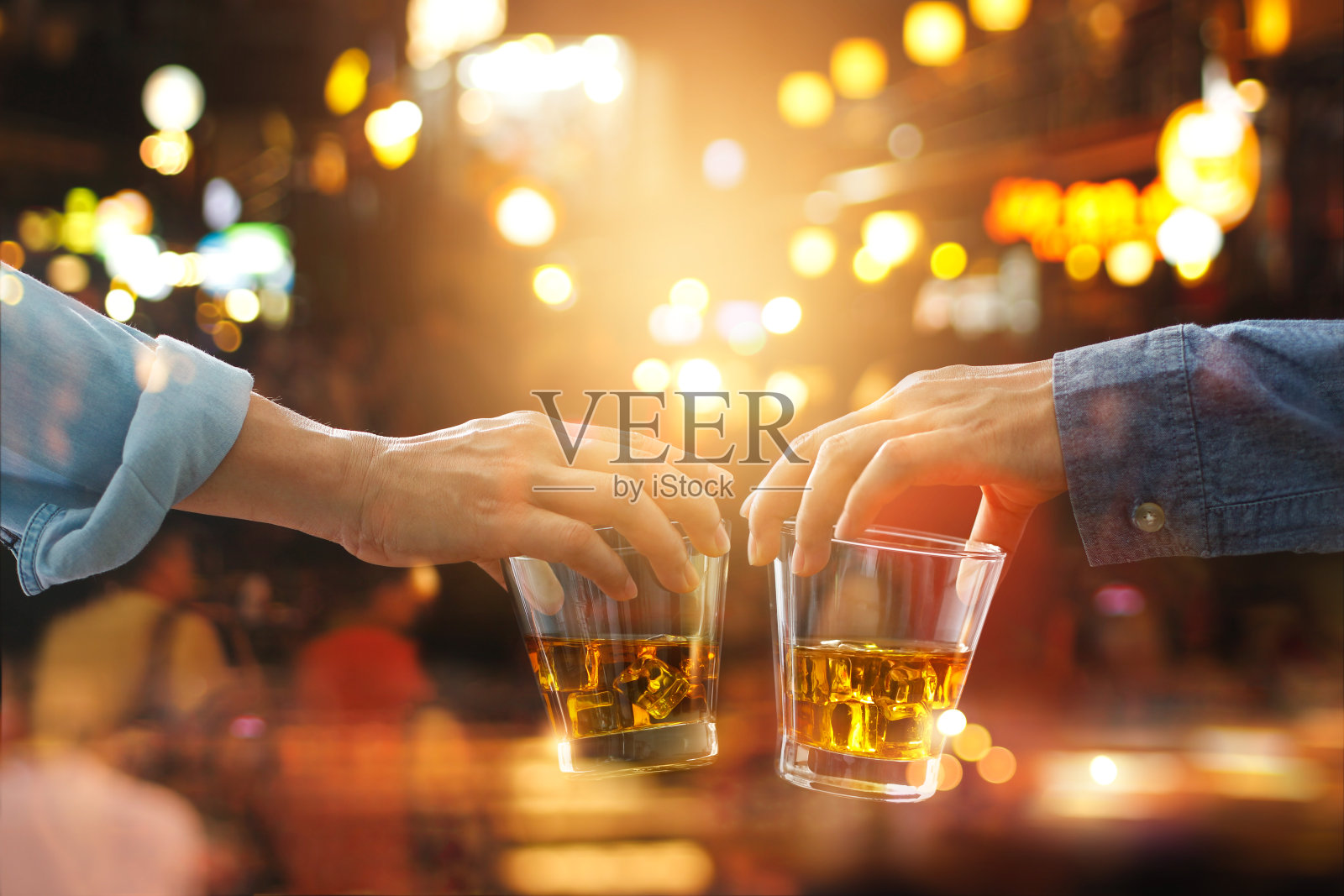 干杯碰杯的朋友与波旁威士忌酒在派对之夜工作后的彩色背景照片摄影图片