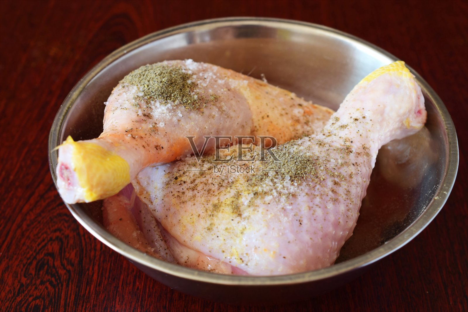 鸡腿放在一个金属碗里，加盐和胡椒，醋。照片摄影图片