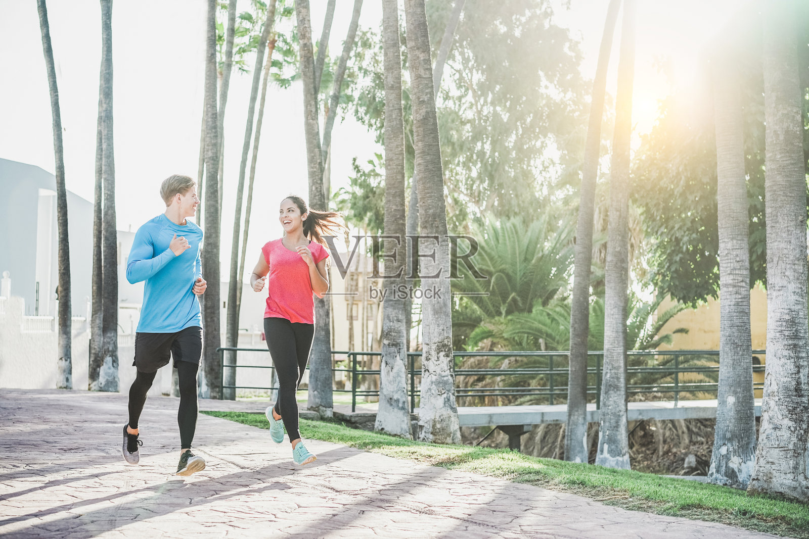 健身的年轻夫妇在户外跑步，以手掌为背景-运动快乐的人在热带地区训练-健康的生活方式，幸福，慢跑和活力的概念-温暖过滤器照片摄影图片