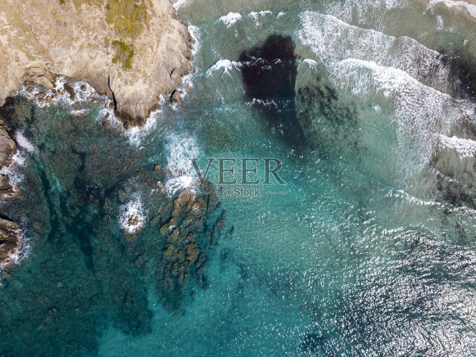 海上岩石的鸟瞰图。从上面俯瞰海床，透明的海水。游泳者，游泳者浮在水面上照片摄影图片
