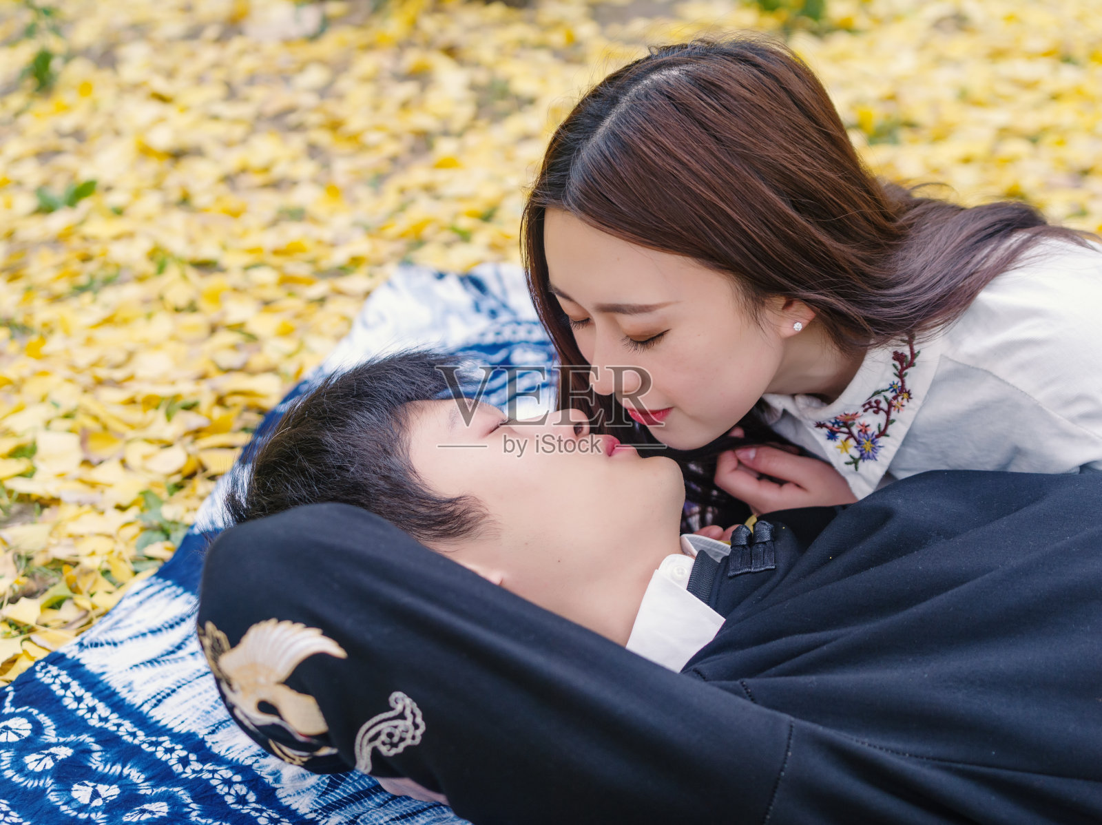 一对中国年轻人的肖像躺在铺满金色银杏叶的秋日地面上，准备亲吻，充满了爱，恋人的概念。照片摄影图片