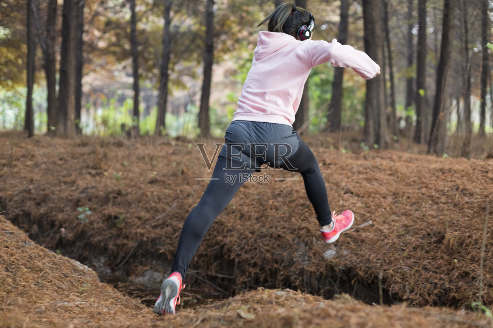 年轻的女运动员在公园里跳过沟渠照片摄影图片
