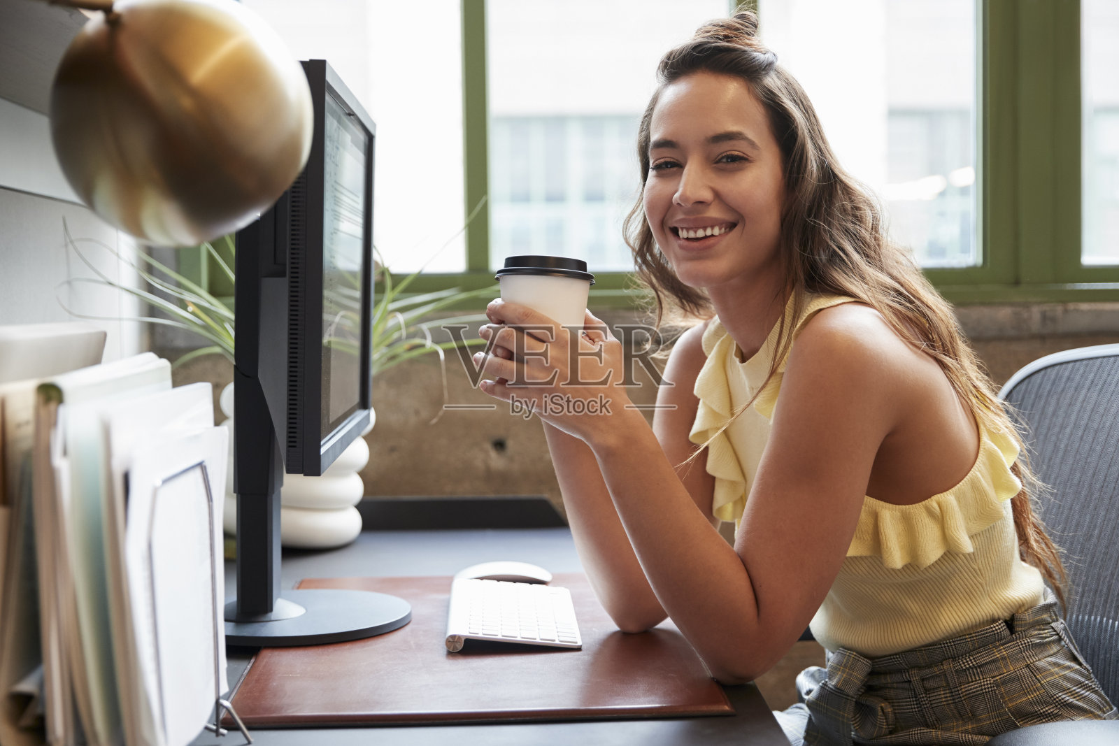 一个女人坐在办公室里，拿着咖啡对着镜头微笑照片摄影图片