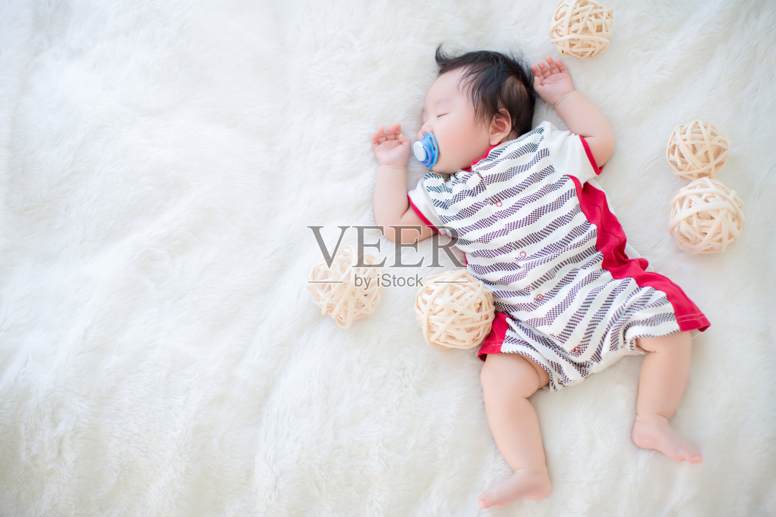 可爱的婴儿吸着奶嘴，睡在柔软的白色地毯上。照片摄影图片