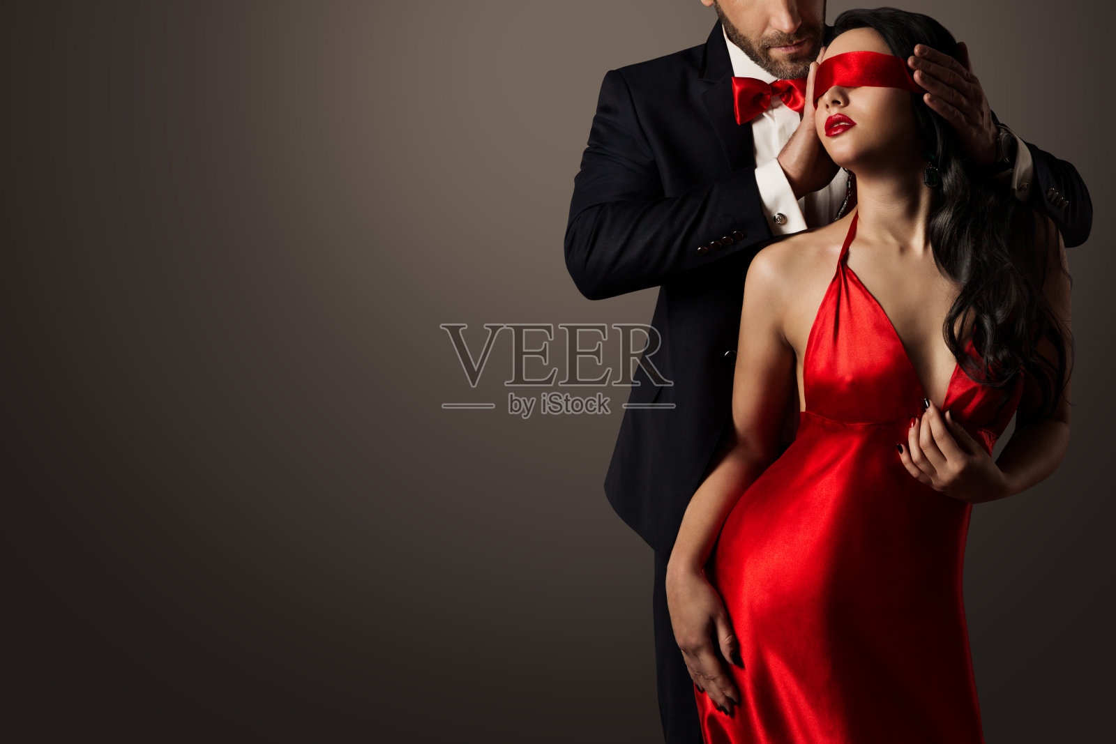 情侣爱吻，性感的蒙住眼睛的女人跳舞在红色的裙子，优雅的男人在西装照片摄影图片