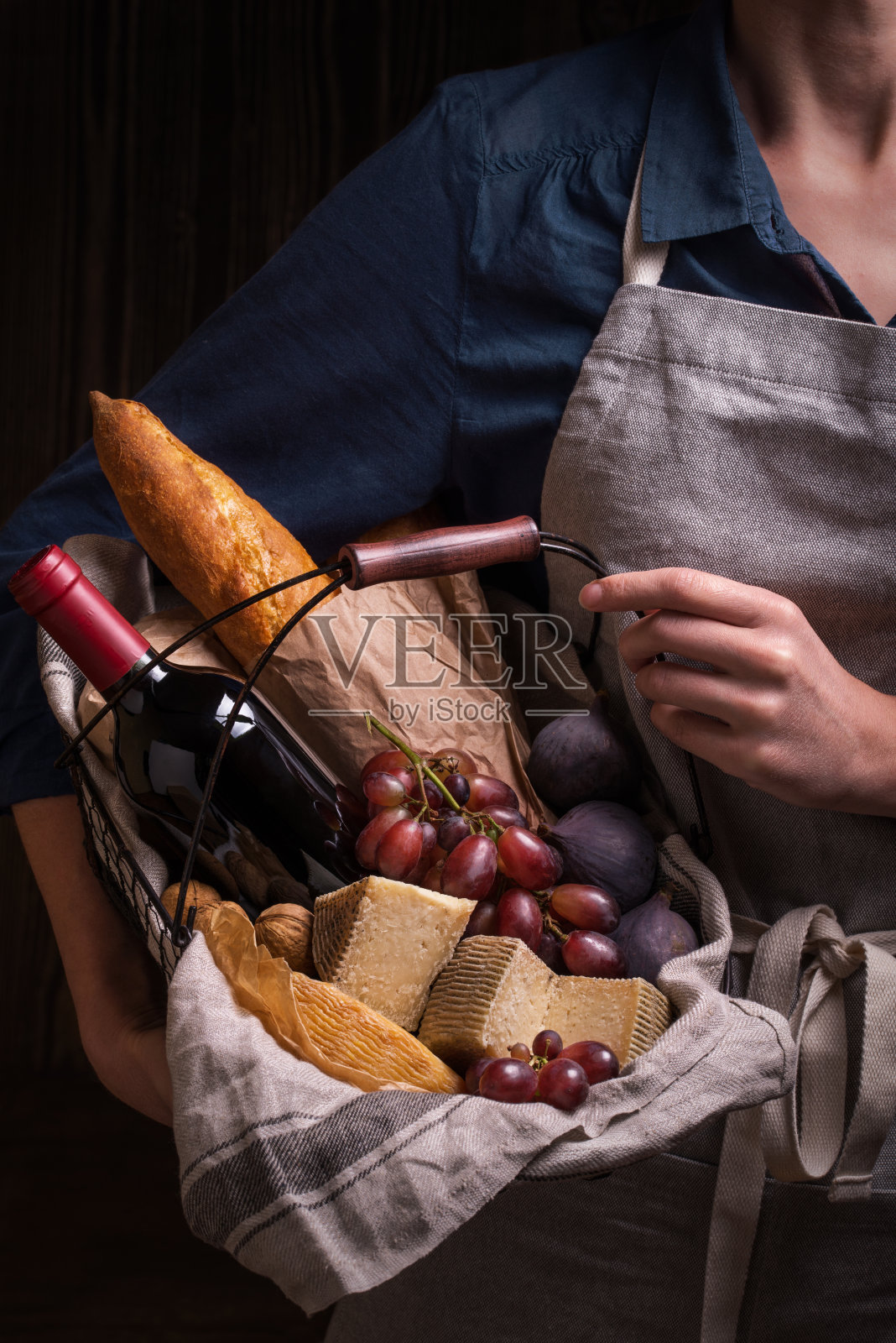 女人拿着一个篮子，里面装着奶酪，葡萄酒，水果和法棍面包照片摄影图片