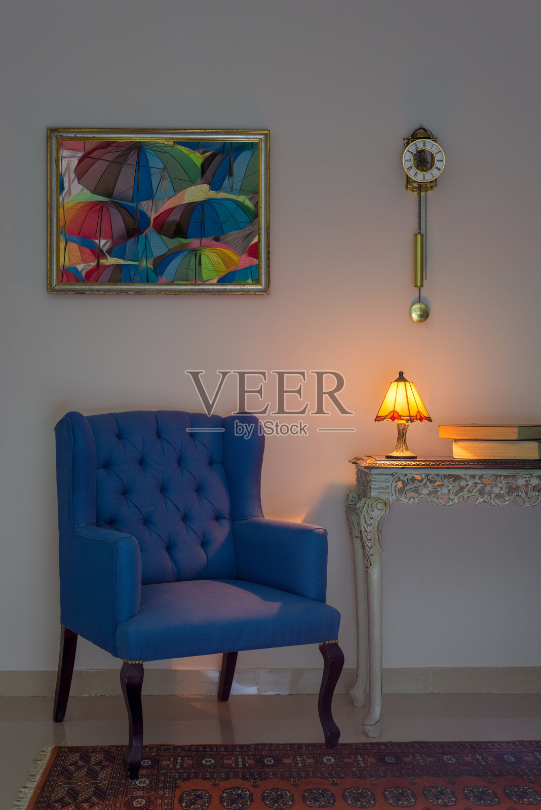 室内构图有蓝色扶手椅、古色古香的米色木桌、照明台灯、书籍、摆钟和橙色装饰的地毯照片摄影图片