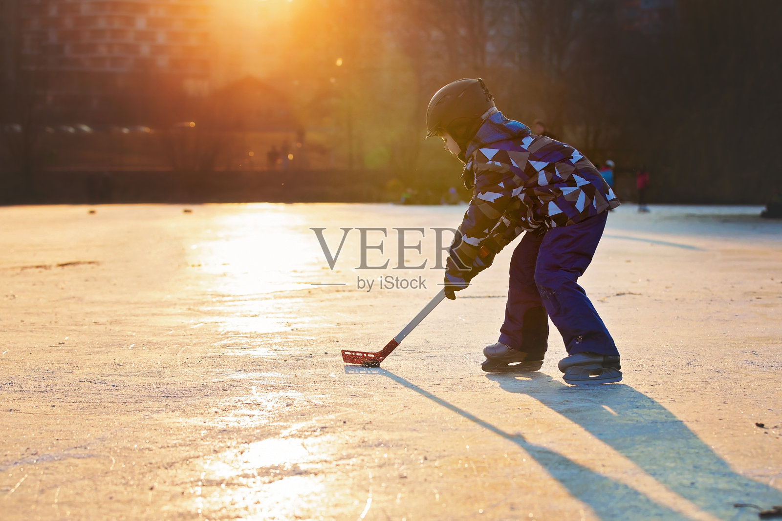 孩子们在公园里冰封的湖面上打曲棍球和滑冰，冬天的日落时分照片摄影图片
