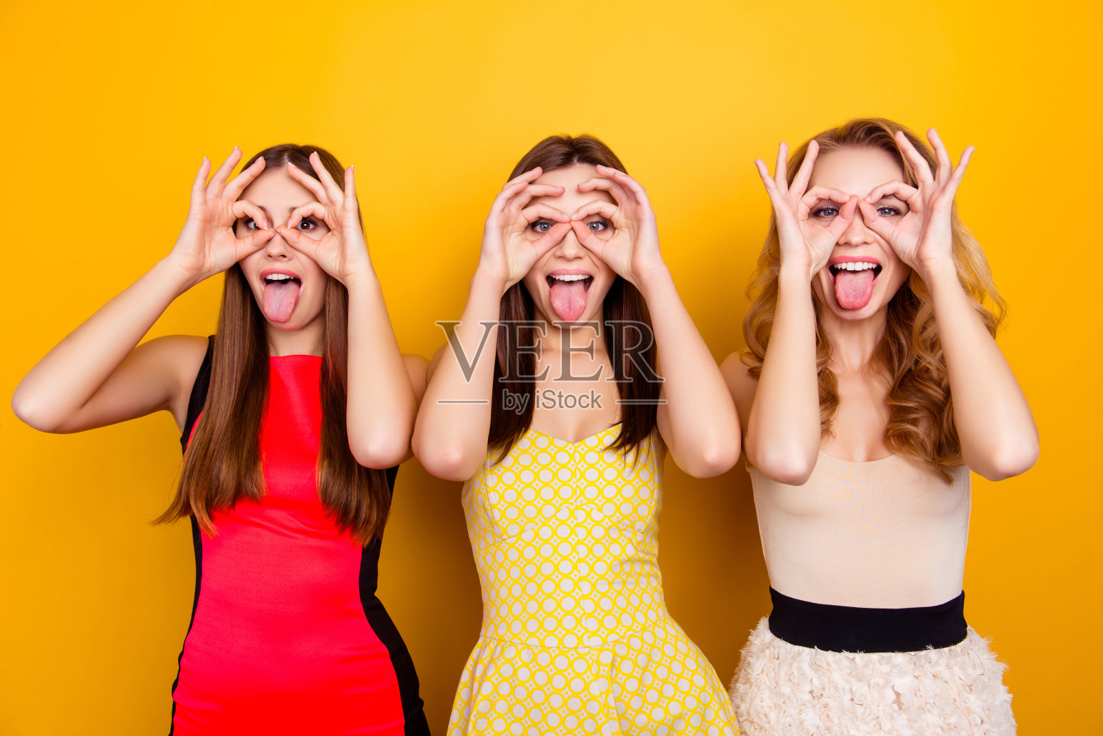 三个漂亮的，迷人的，迷人的，漂亮的，时髦的，疯狂的女孩展示望远镜，手指，手和手势舌头，愚蠢的黄色背景照片摄影图片