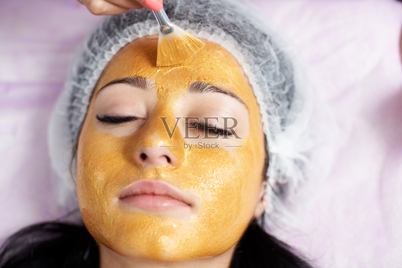 脸部特写的一个女性客户的美容院与一个金色的面具。日常美容和皮肤护理。照片摄影图片