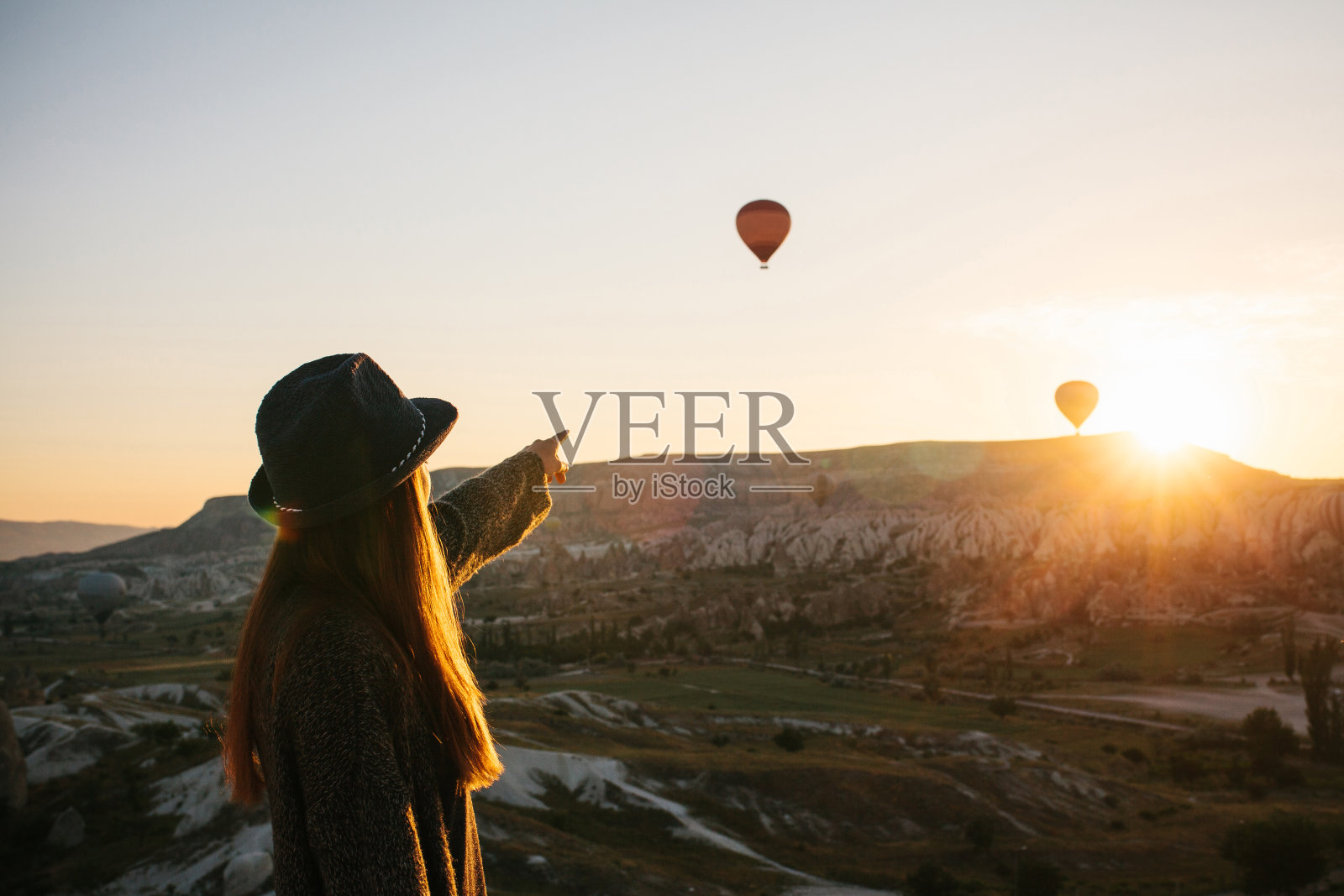 土耳其卡帕多西亚上空，一名戴着帽子的女游客正在欣赏热气球。令人印象深刻的景象。照片摄影图片