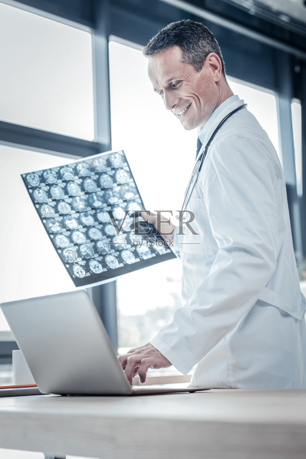 满意愉快的医生看着笔记本电脑和拿着x光扫描。照片摄影图片
