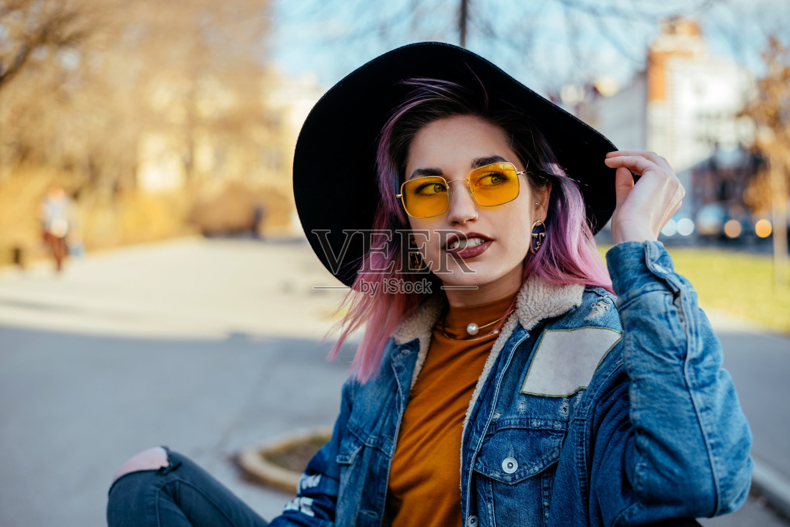 漂亮的都市女孩戴着帽子和黄色太阳镜坐在城市公园里。照片摄影图片