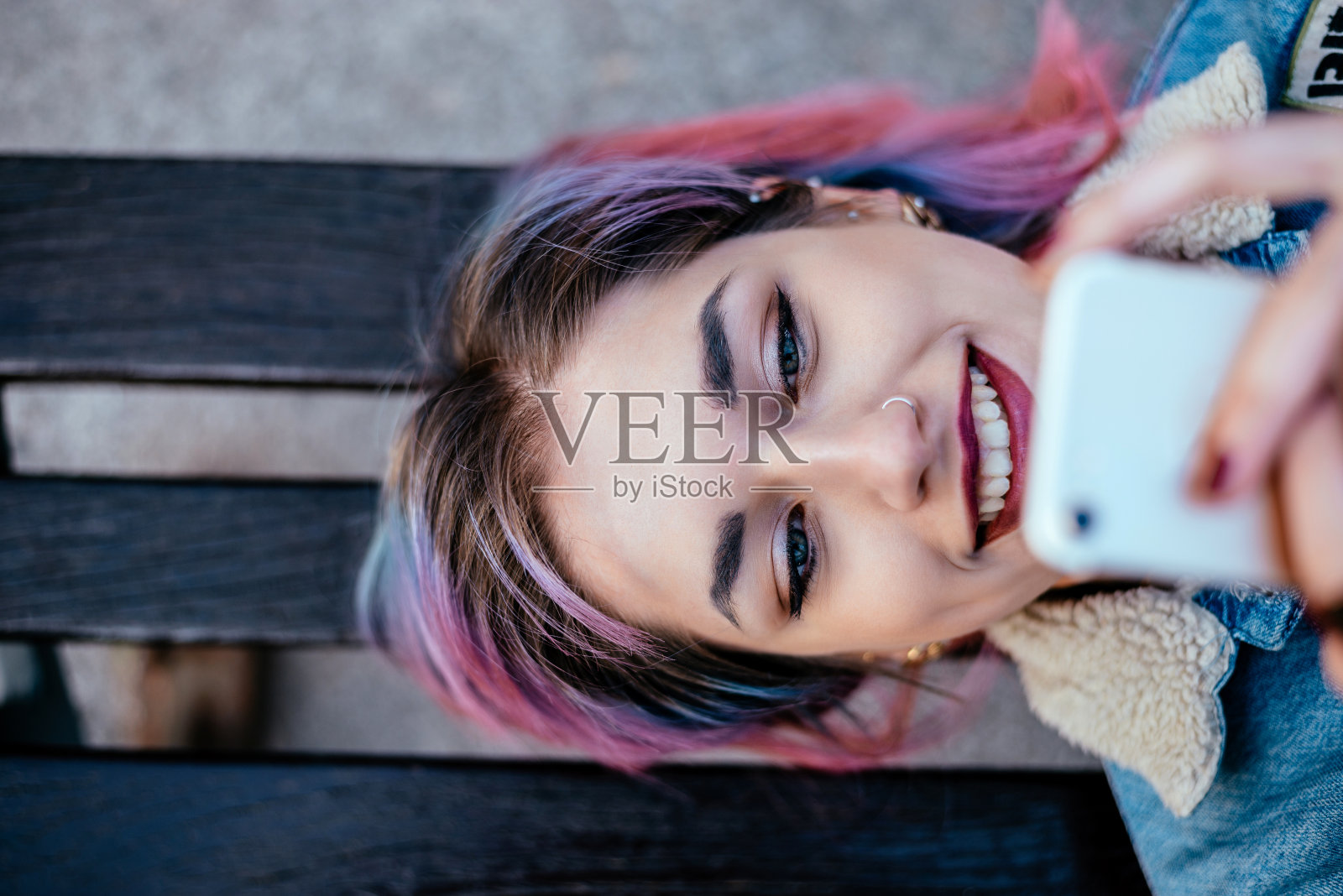 一个微笑的女孩的特写照片染了头发，而躺在长凳上用手机。前视图。照片摄影图片