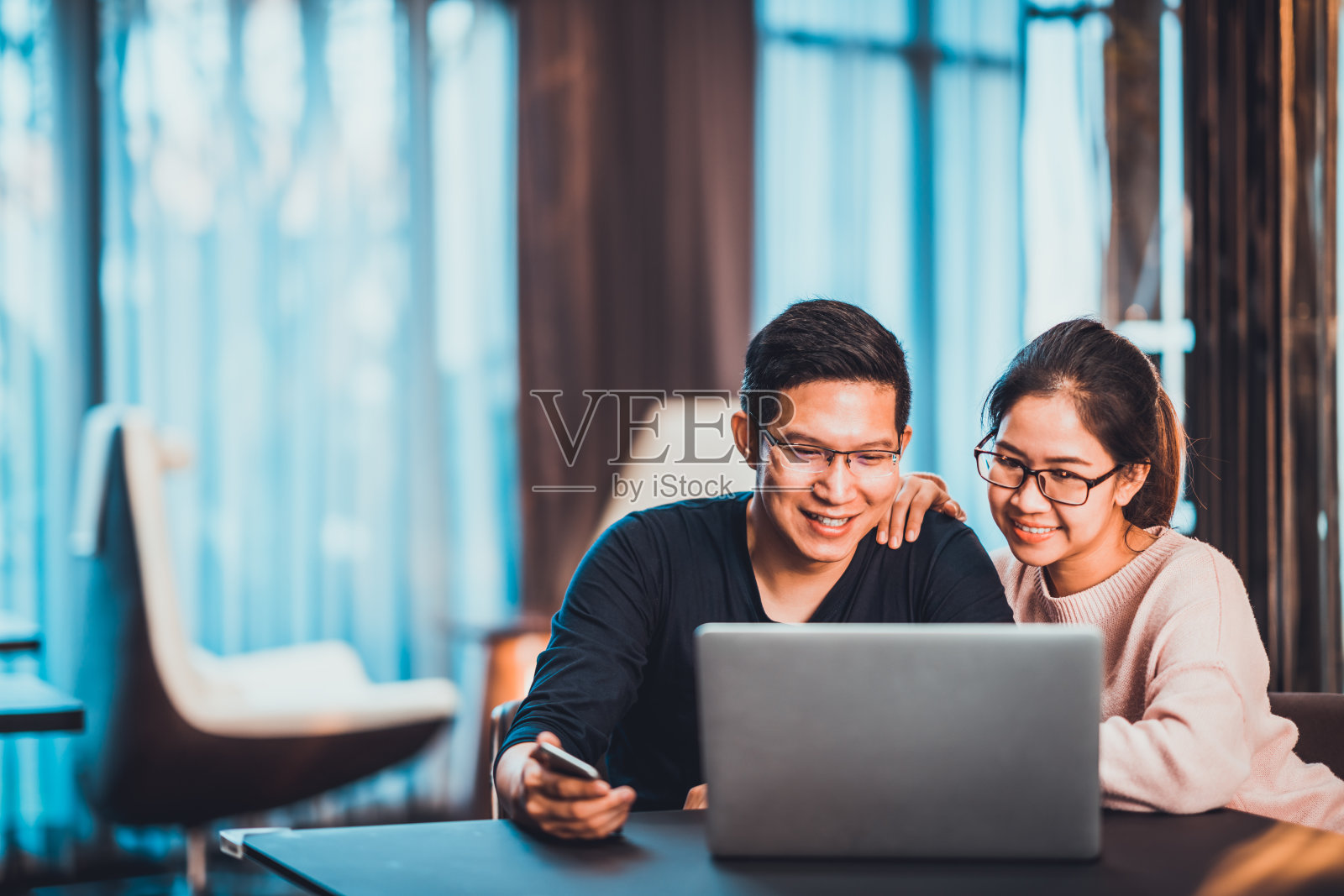 年轻的亚洲夫妇在家里或有复印空间的现代办公室使用笔记本电脑一起工作。创业的家庭企业，中小企业企业家，商业伙伴，爱情关系，或自由职业者的概念照片摄影图片