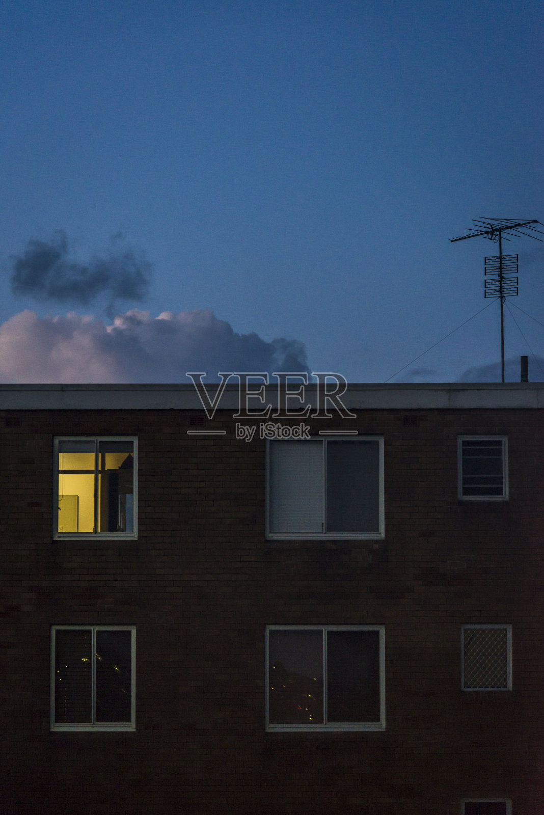 傍晚时分，澳大利亚悉尼东郊库吉，一间现代的、没有特色的公寓里的一扇窗户被电视天线照亮照片摄影图片