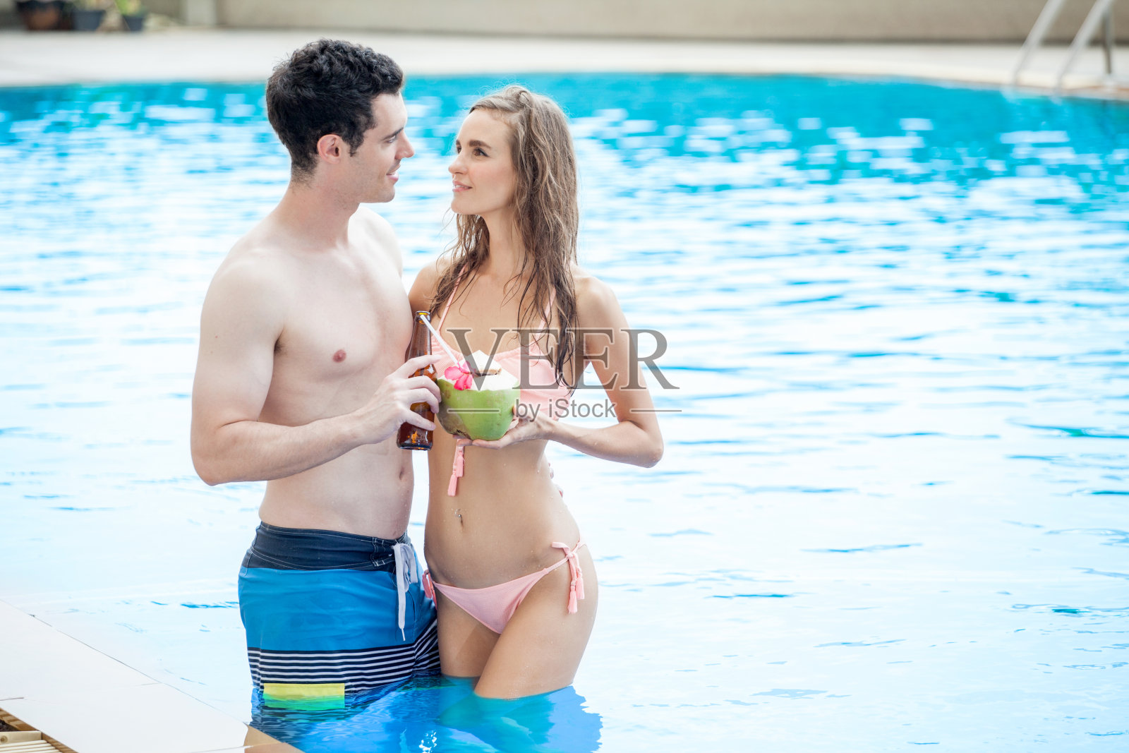 美丽的年轻夫妇相爱在游泳池和喝鸡尾酒照片摄影图片