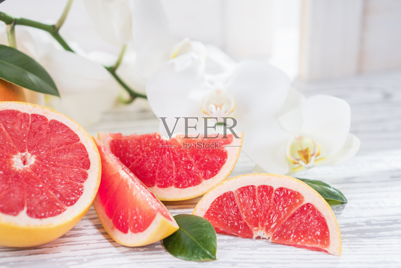 百叶窗对面质朴的白色木桌上放着新鲜的红葡萄柚和葡萄柚片。健康饮食理念。照片摄影图片