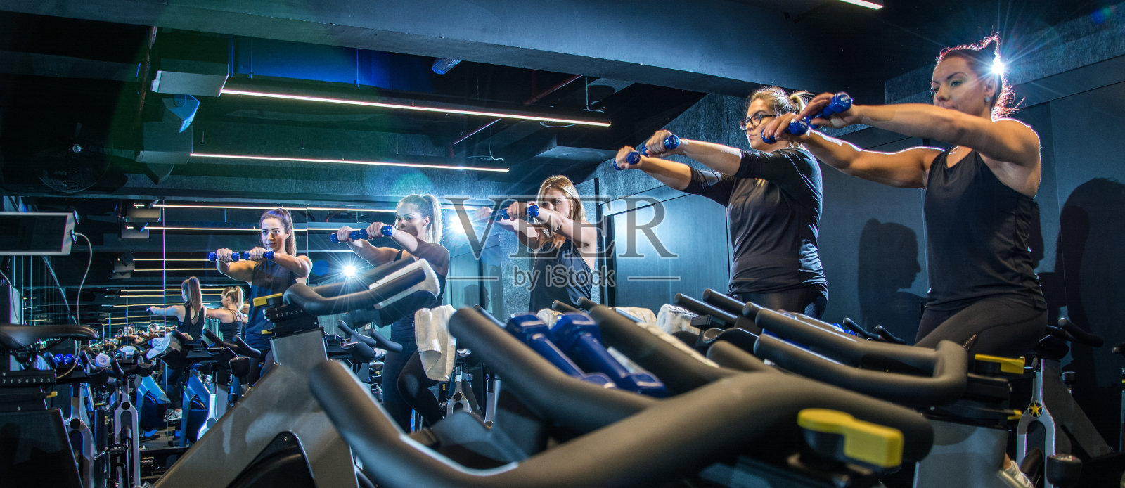 全景运动女孩做举重锻炼，同时骑健身自行车在健身房照片摄影图片