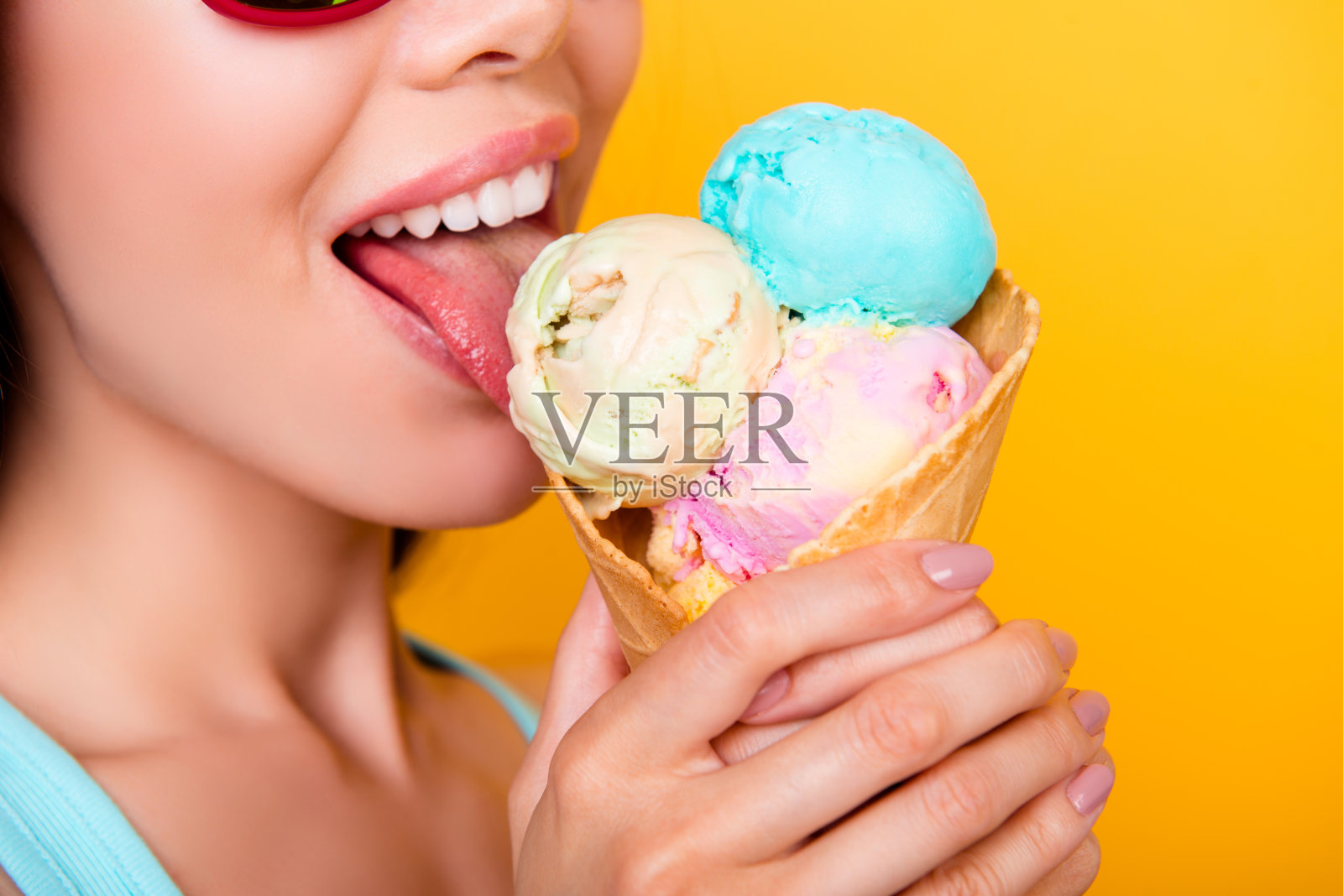 小女孩戴着墨镜，在黄色的背景上舔着三勺不同口味的美味冰淇淋照片摄影图片