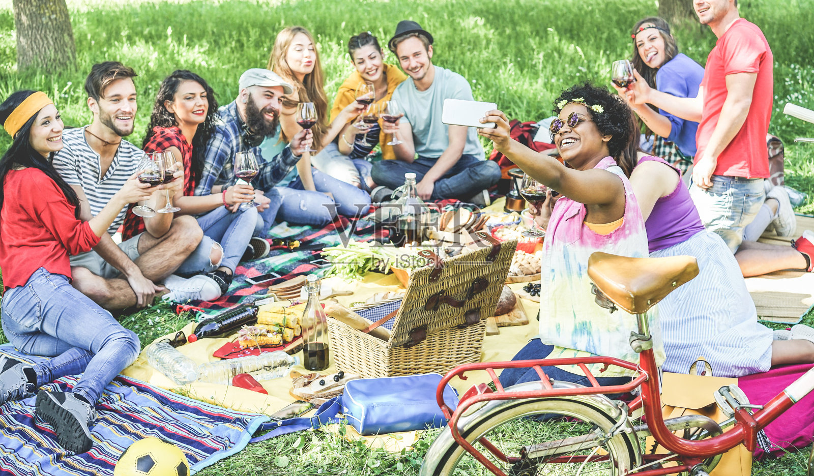 快乐的不同的朋友在户外野餐聚会自拍-年轻人喝葡萄酒，吃和与科技潮流一起的乐趣-夏季概念-关注非洲女孩的脸照片摄影图片