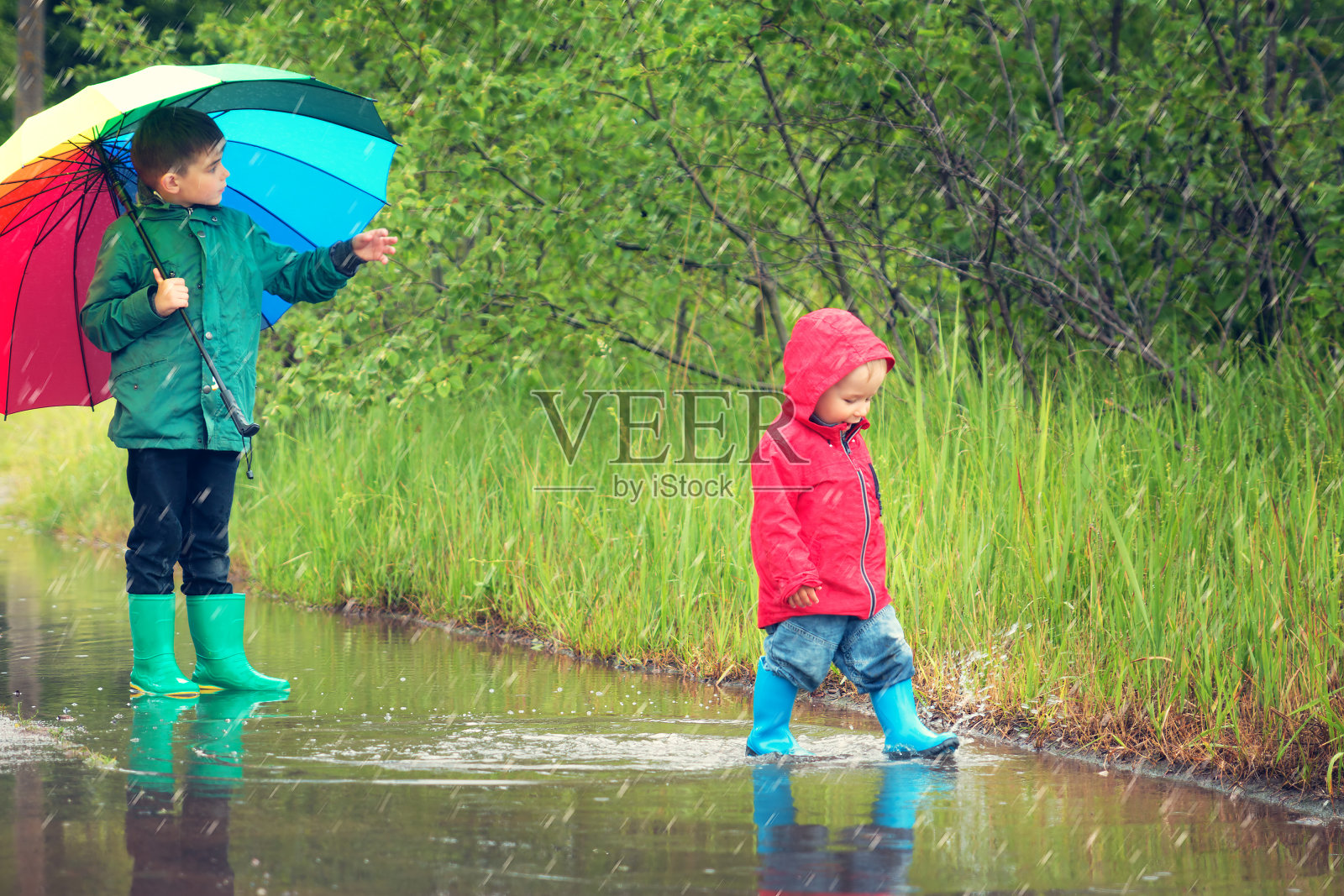 孩子们穿着雨靴在水坑里行走照片摄影图片