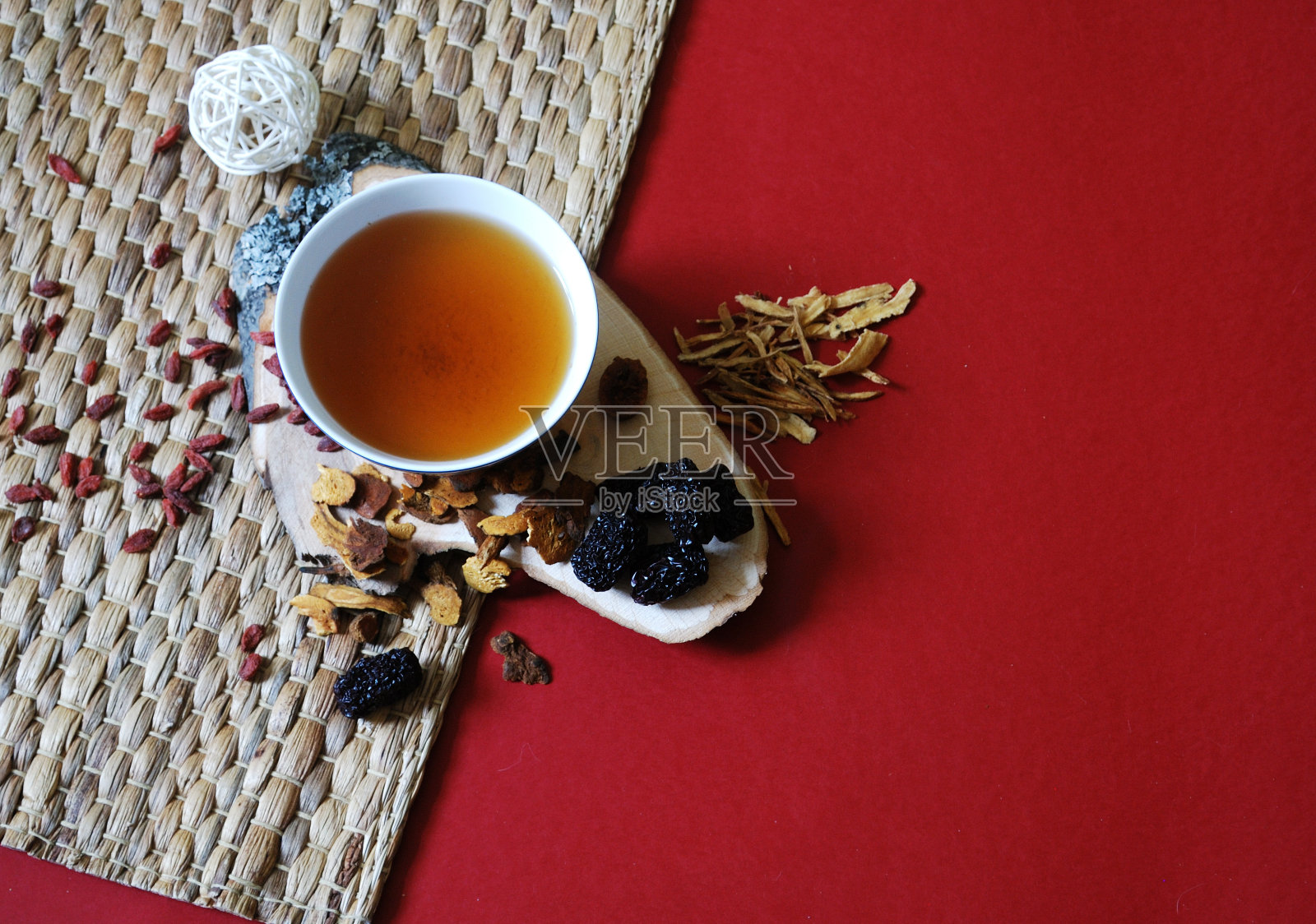 枸杞、红枣、黄芪片配一碗香草茶在红色背景上。前视图。照片摄影图片