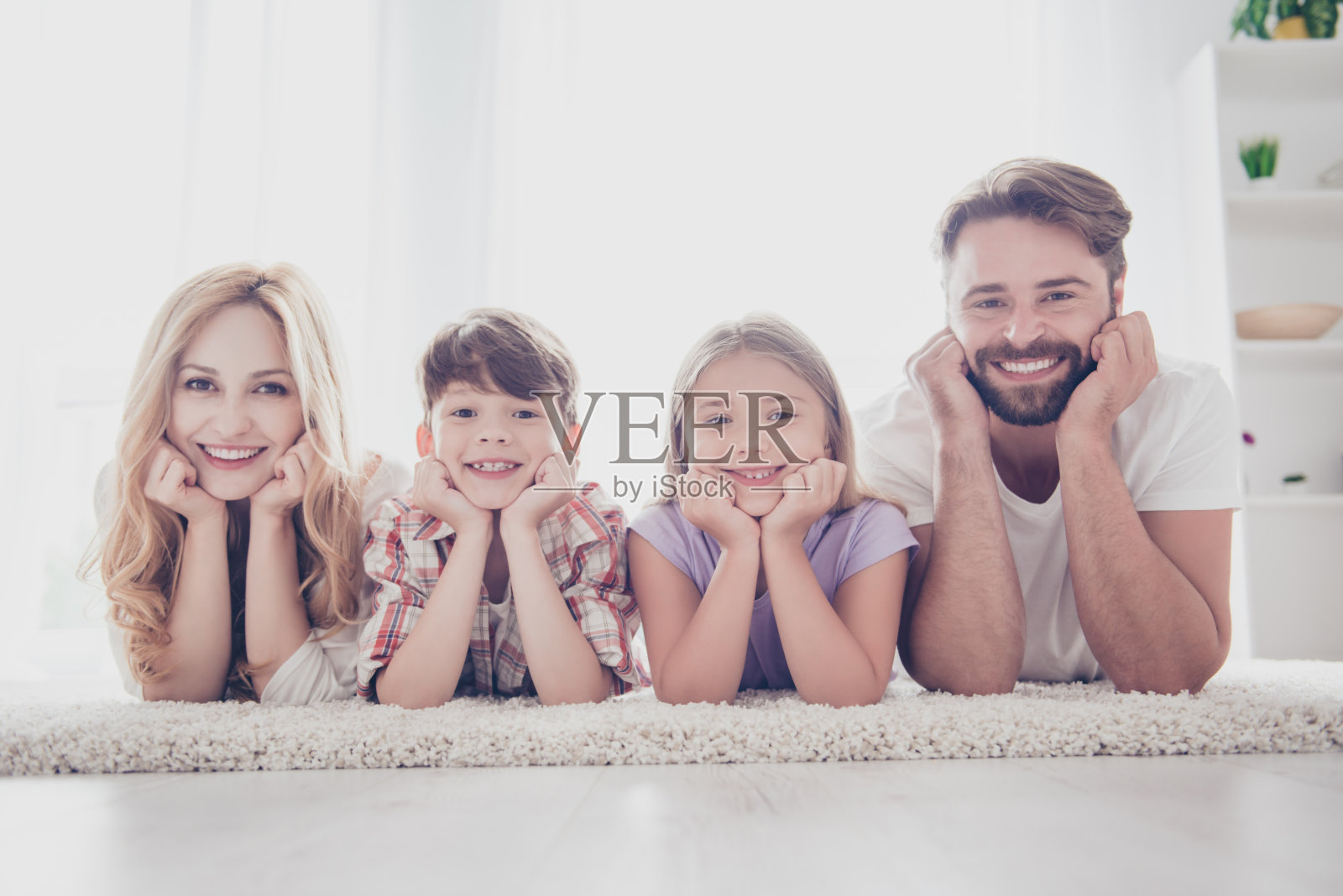 幸福的家庭的概念。四个亲戚躺在地板上的地毯上，头抱着胳膊，微笑着，在家里照片摄影图片