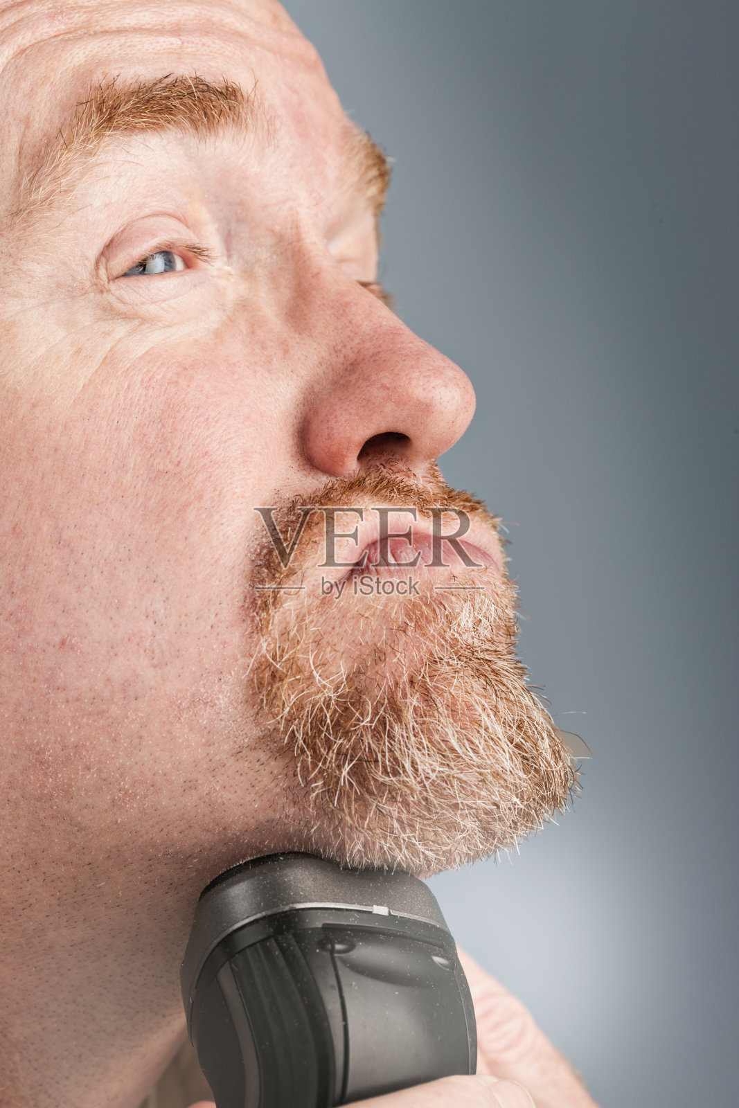 用电动剃须刀修胡子的男子拉了一张脸照片摄影图片